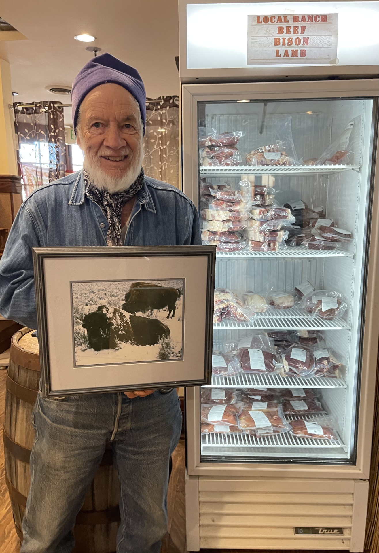 Man with a beard standing next to a meat cooler holding a picture of buffalo