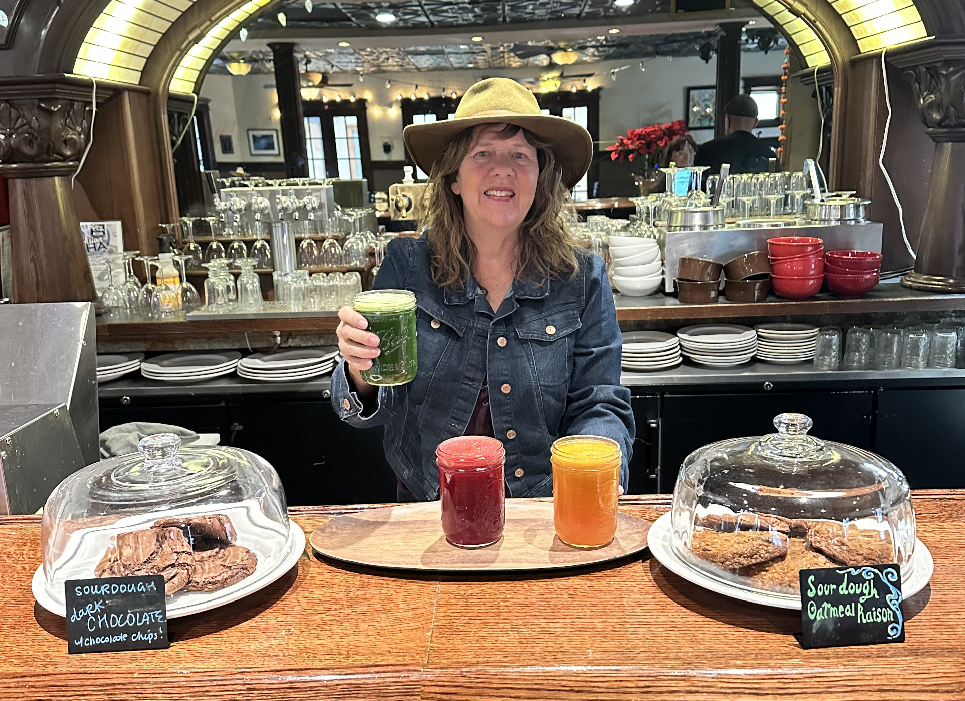 Woman standing at a bar with fresh squeezed orange and beet juice and holding a green juice in her hand
